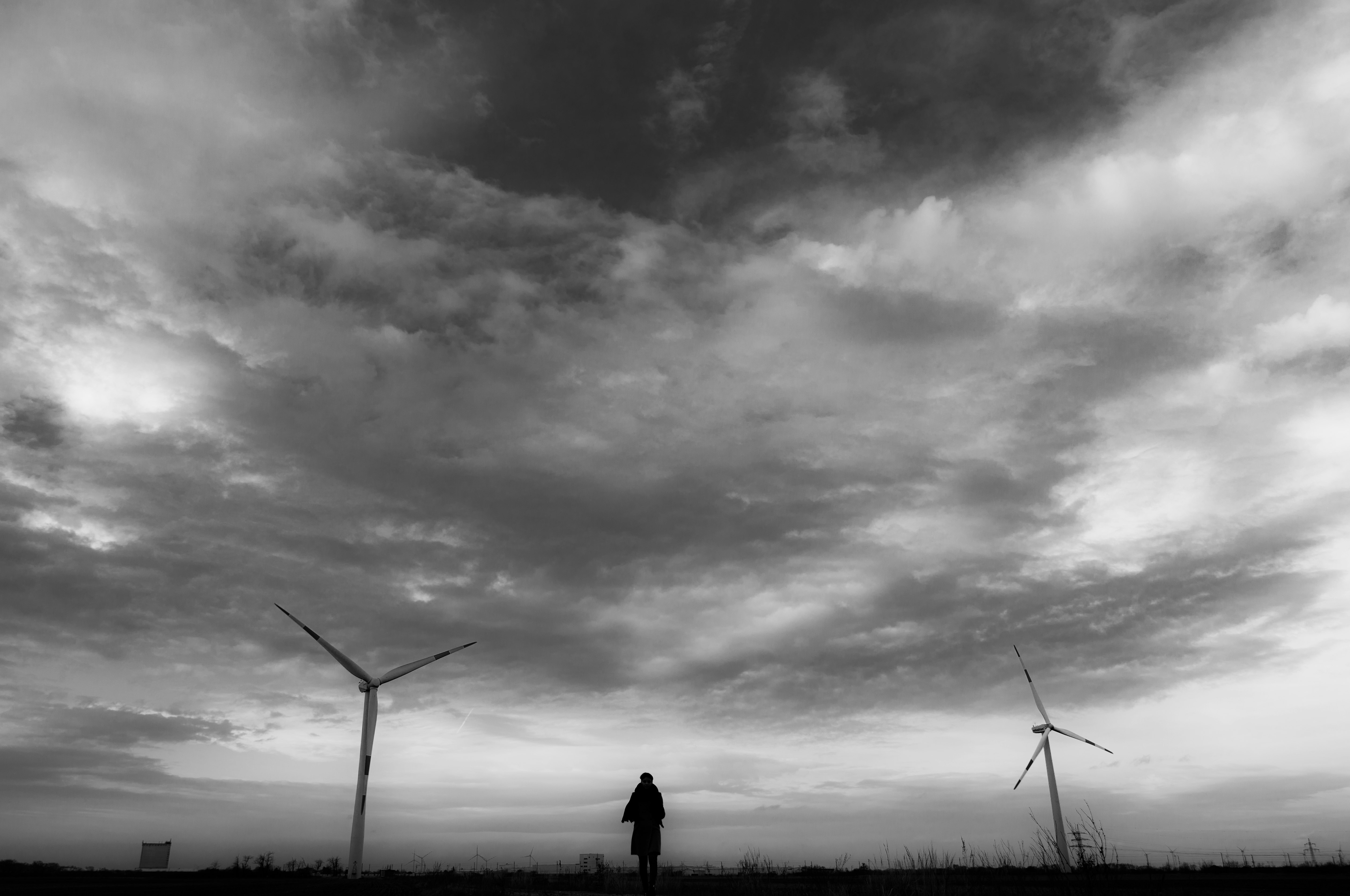 silhouette of person standing near wind turbines under cloudy sky during daytime